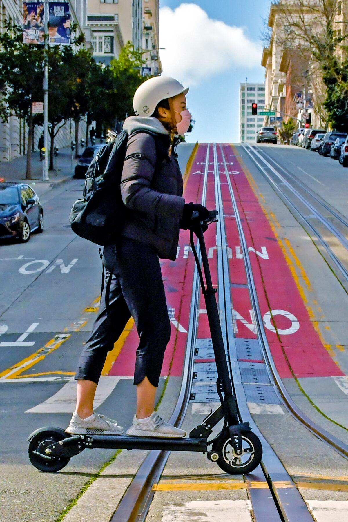 A woman rides a scooter on an empty California Street in San Francisco 