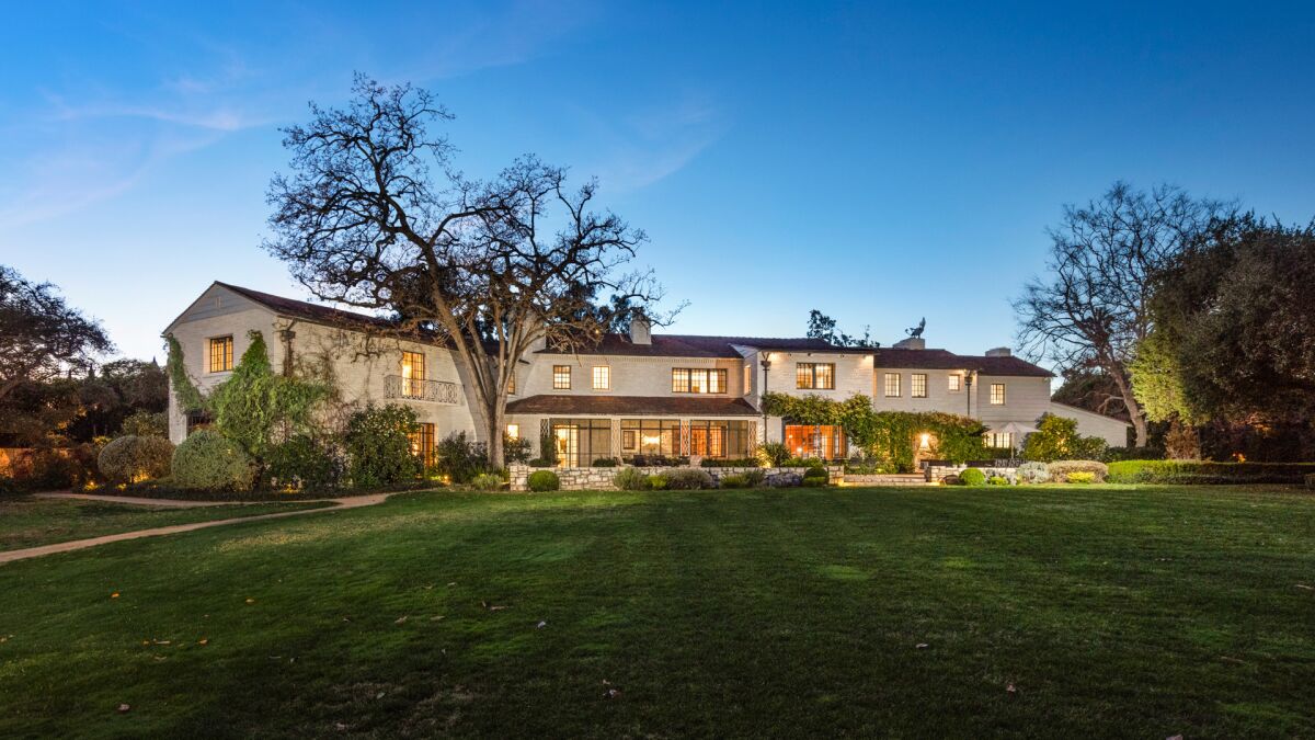 A photo of a large two-story mansion surrounded by grass with trees