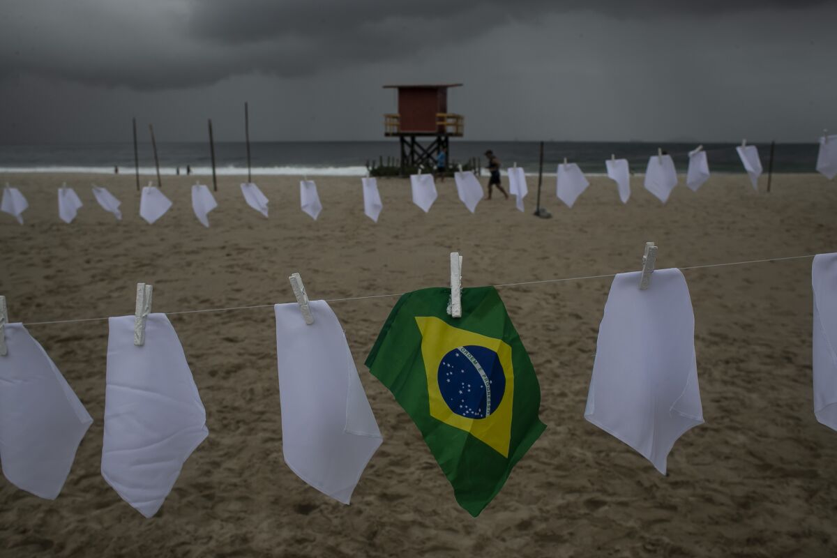 A Brazilian flag hangs on a clothesline on Copacabana beach amid white scarves that represent those who have died of COVID-19 in Rio de Janeiro, Brazil, Friday, Oct. 8, 2021. The action was organized by the NGO "Rio de Paz" to protest the government's handling of the pandemic as the country nears a total of 600,000 COVID-19 related deaths. (AP Photo/Bruna Prado)