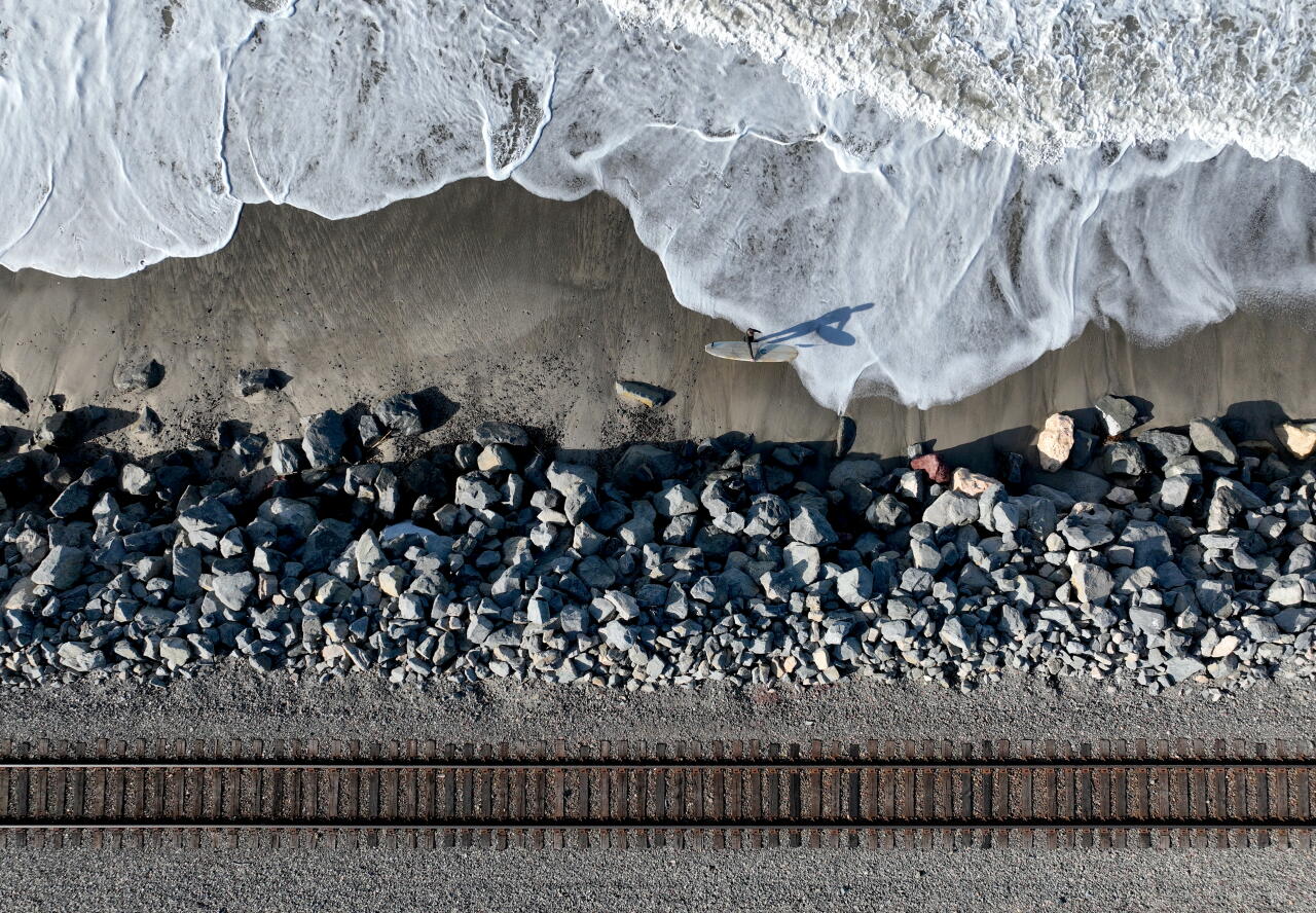 A surfer walks near train tracks north of the San Clemente Pier.