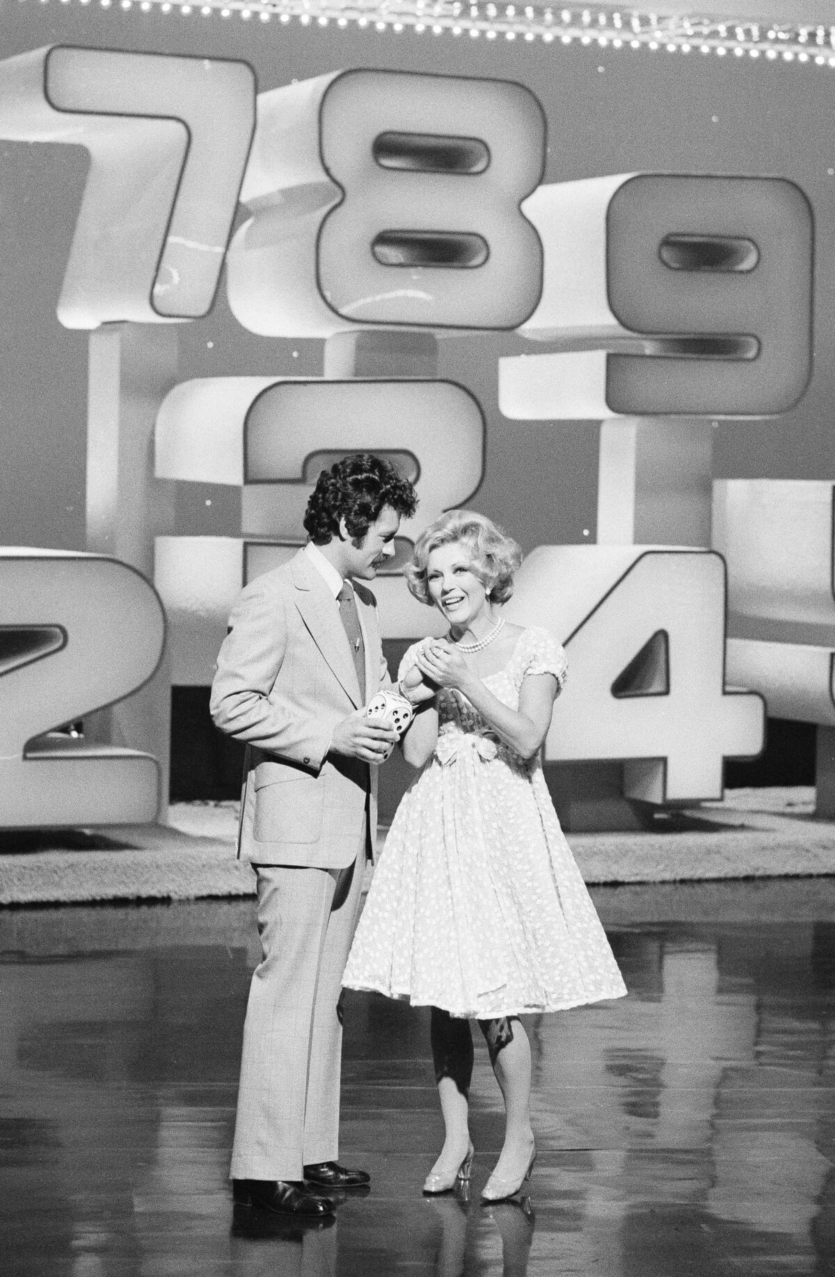 Black-and-white photo of Alex Trebek and Ruta Lee on the set of the 1970s game show "High Rollers."