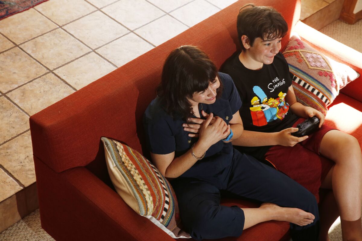 A woman puts her hands over her heart while playing video games with a boy.