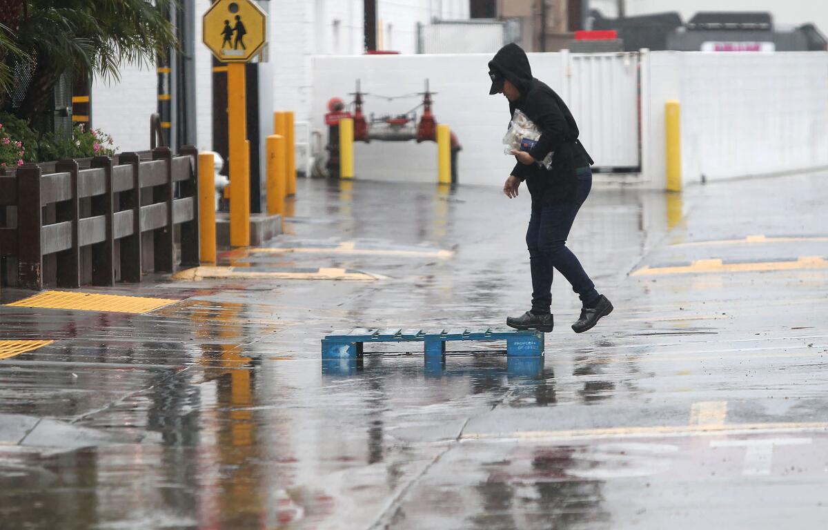A wood pallet serves as a bridge for a worker at a Sprouts market in Newport Beach as rainwater runs down an alley behind the store Wednesday.