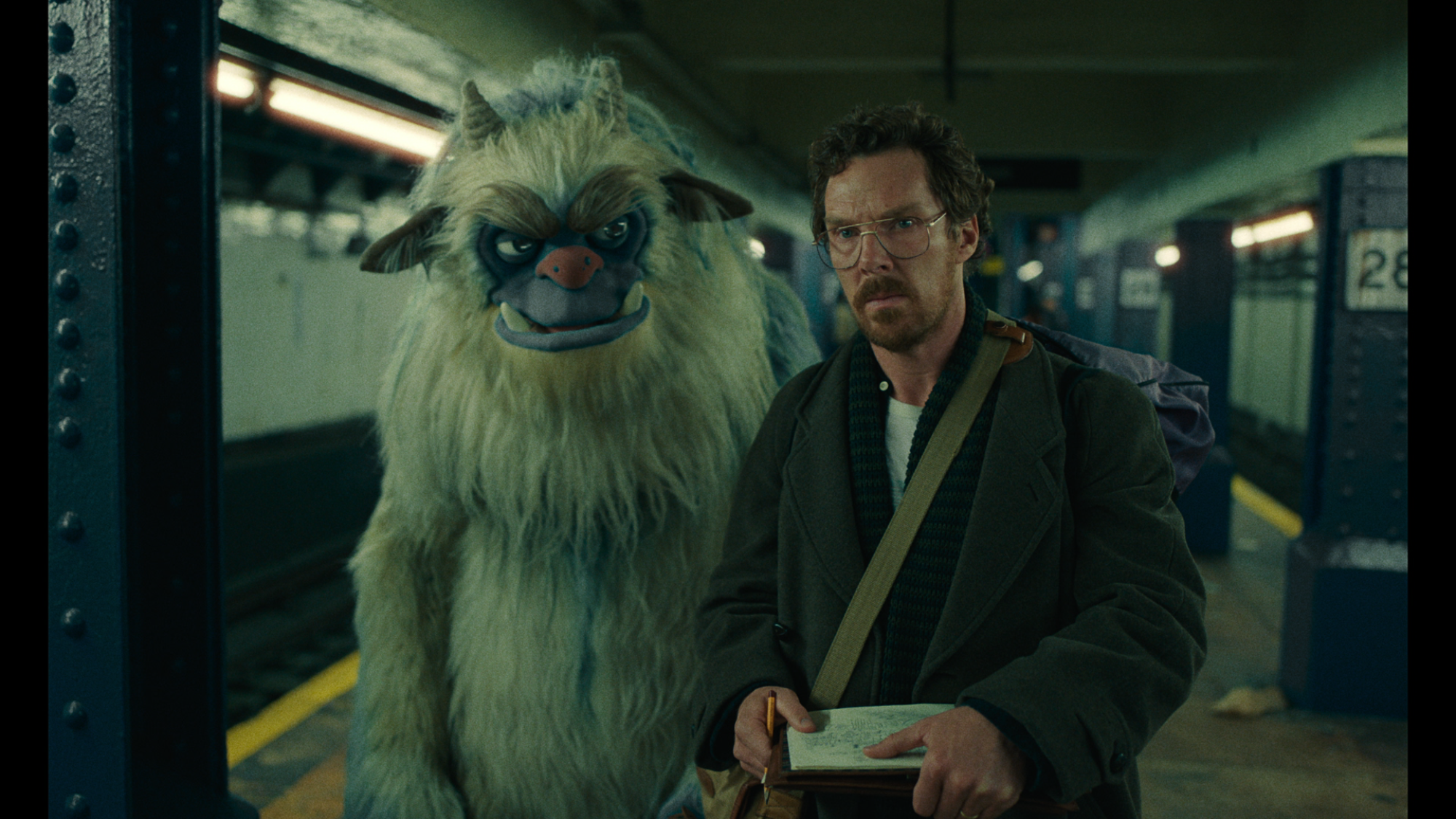 A life-size monster puppet walking behind a man on a subway platform.