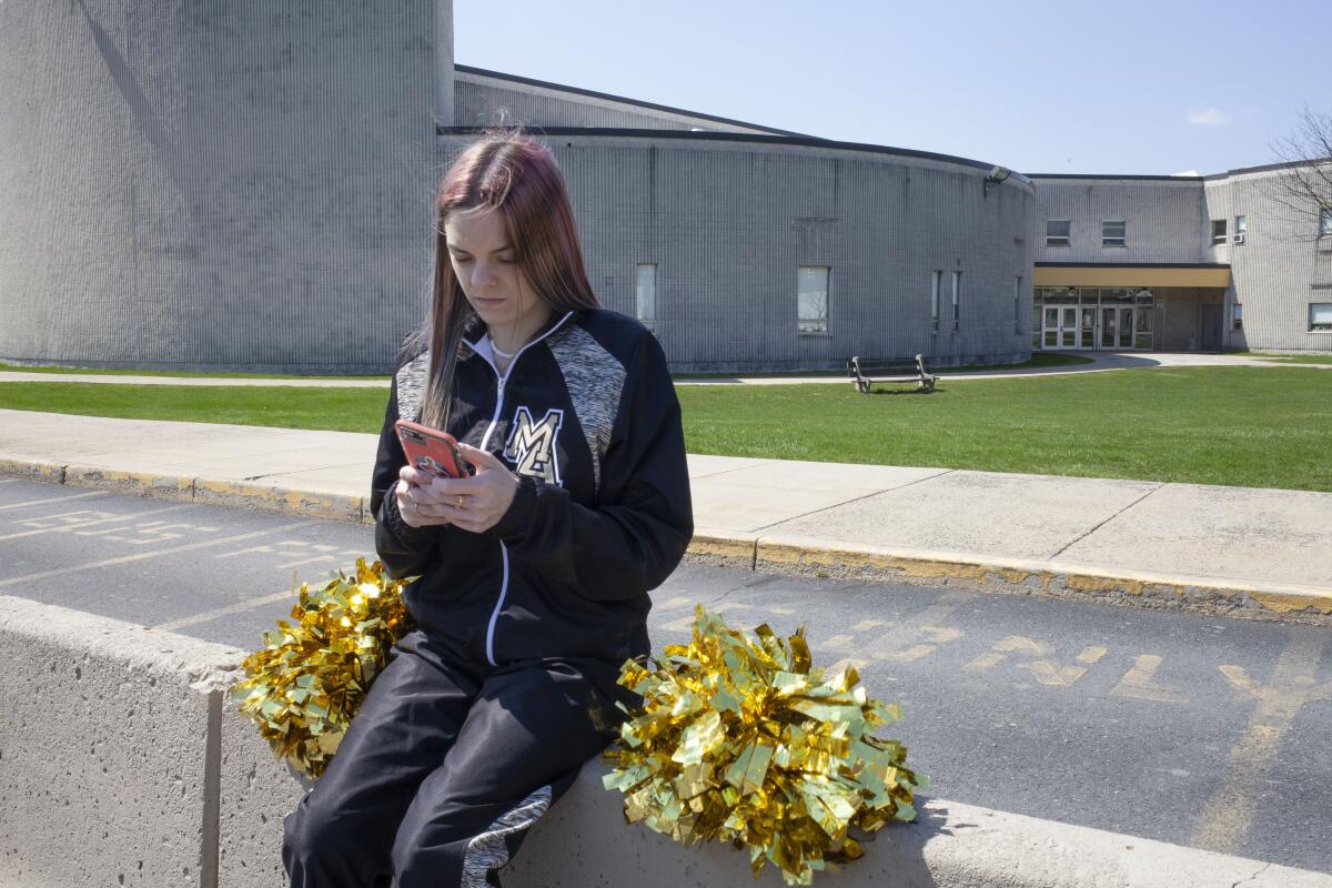 A teenage girl sits on a concrete wall using her smartphone