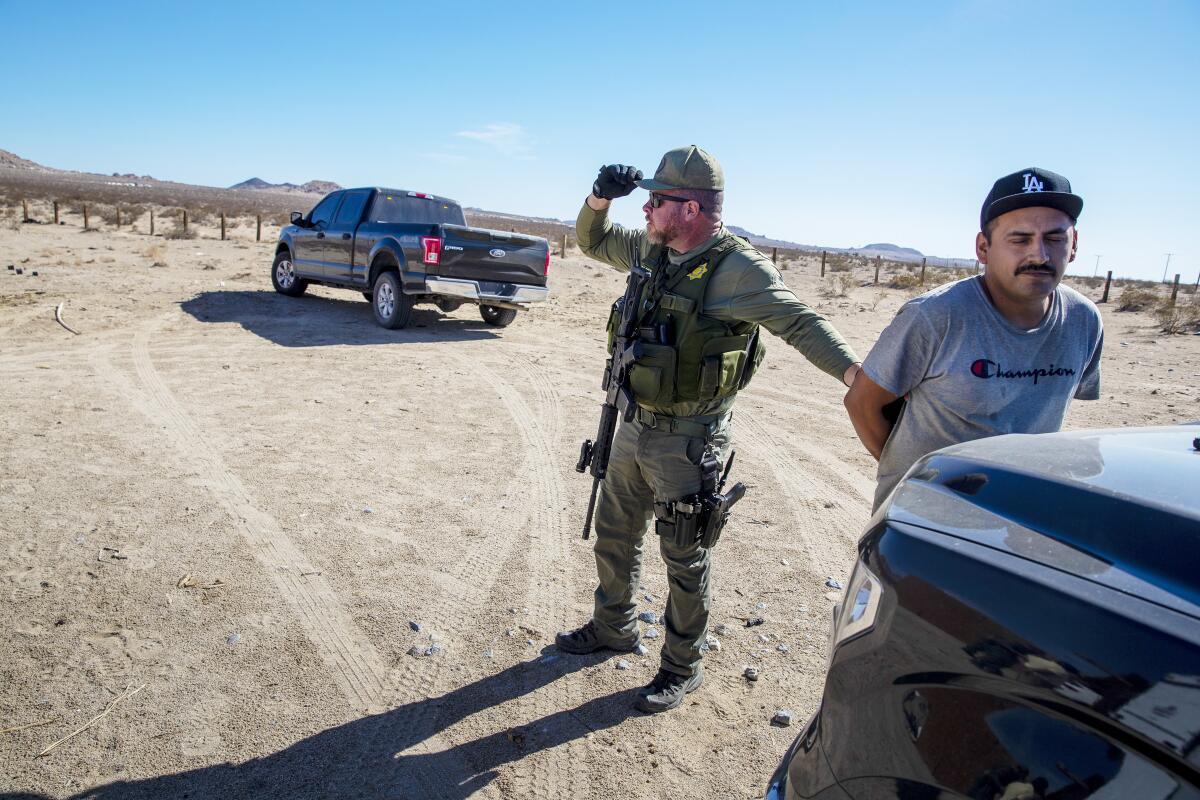A San Bernardino County sheriff's deputy, left, detains a cannabis worker in the Lucerne Valley, CA. 
