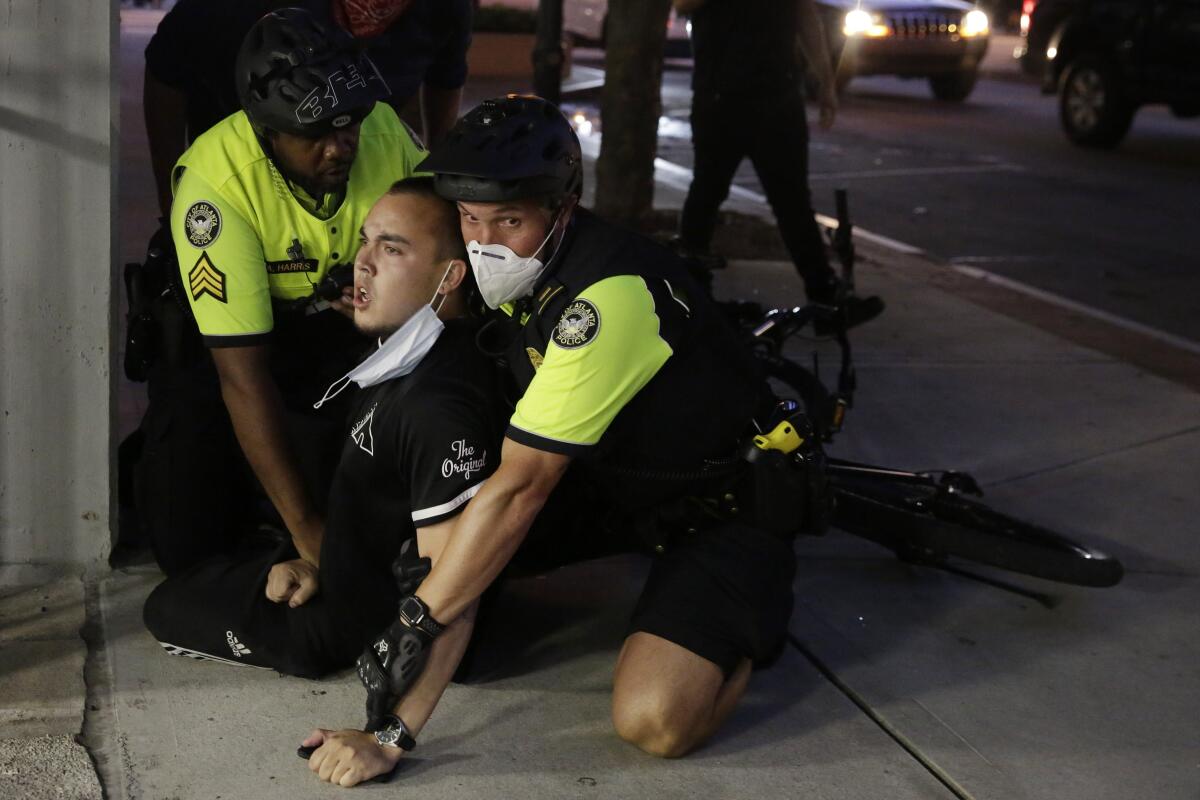 A person is restrained by two police officers on the sidewalk