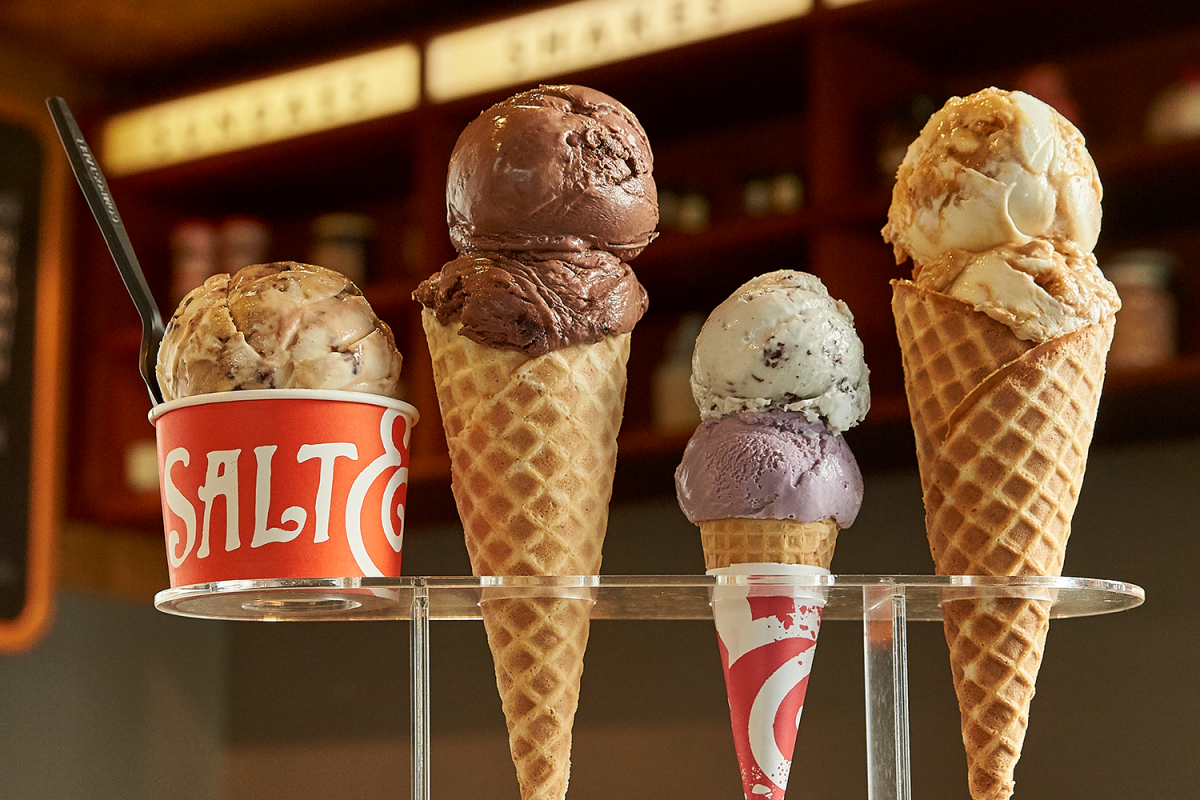 A paper cup and three cones with scoops of ice cream in a rack on a counter