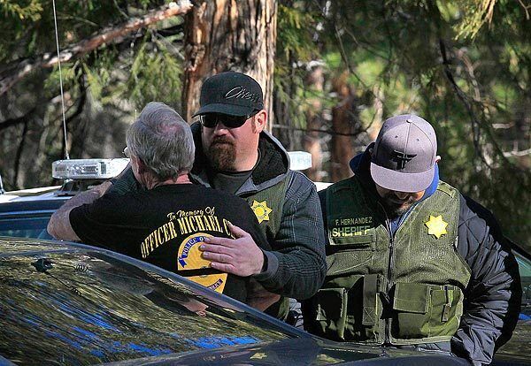 A man wearing a T-shirt in memory of fallen Riverside Officer Michael Crain hugs San Bernardino County deputies at a roadblock near Angelus Oaks.
