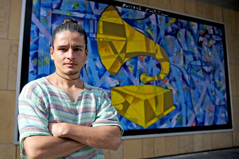 Quetzal Fuerte, 34 of Mexico, who was commissioned to paint a mural on the outside wall of the Grammy Museum, poses in front of the mural, in Los Angeles, on Friday, Nov. 11, 2022.