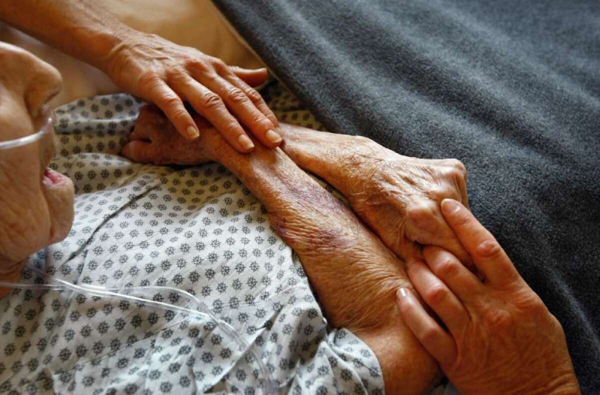 Hospice volunteers are seen caressing the hands of terminally ill patient.