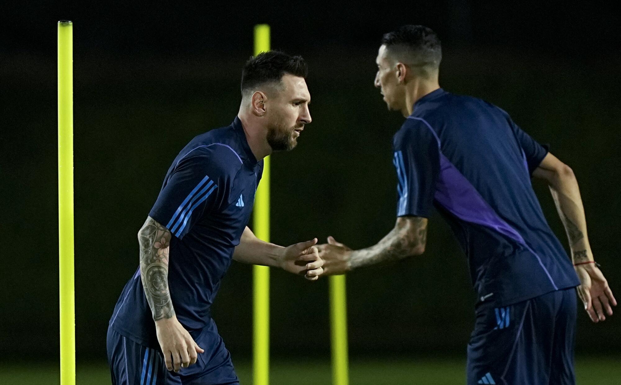 Argentina's Lionel Messi, left, and Angel Di Maria warm up during a training session Thursday in Doha, Qatar.