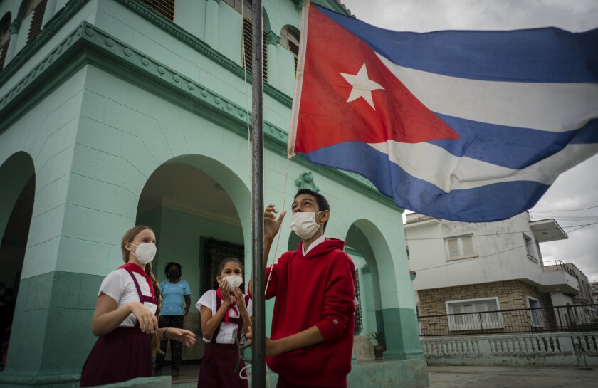 Estudiantes, con mascarilla por la pandemia del coronavirus, arrían una bandera cubana