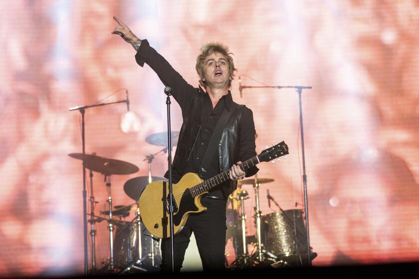 Billie Joe Armstrong wears a a black jacket, pants and shirts as he plays a yellow and black guitar onstage