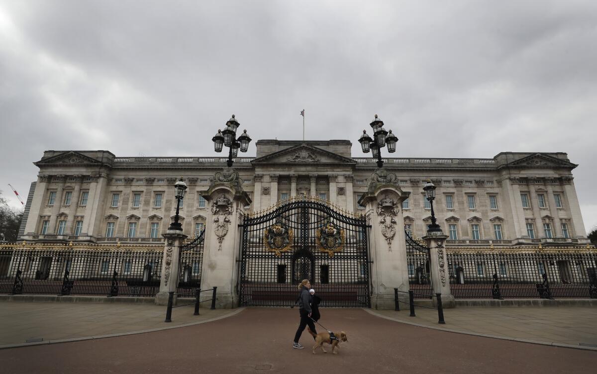 ARCHIVO – Una mujer camina con un perro y un bebé frente al Palacio de Buckingham 