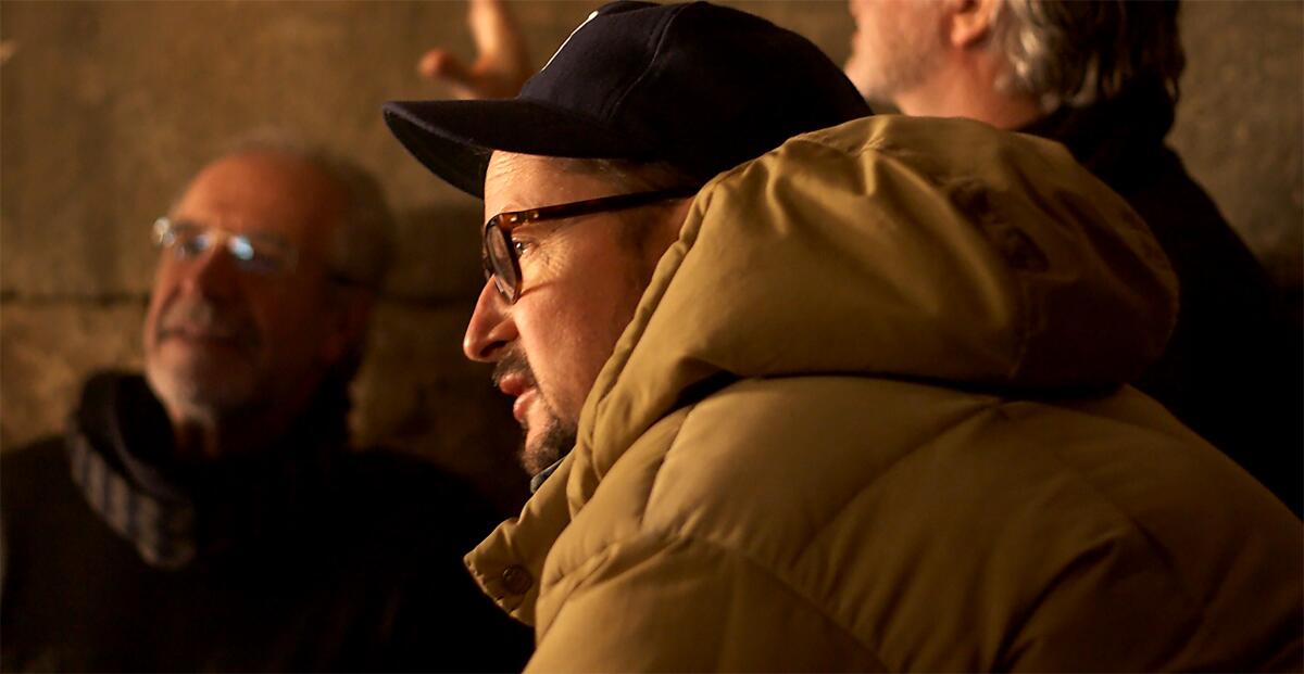 Director Todd Field wears a coat and baseball cap as he talks in a group.