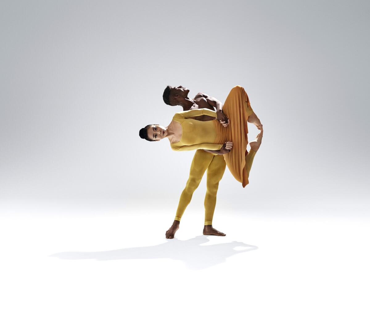 A male dancer, dressed in yellow, suspends a female dancer, also wearing yellow, in a scene from a Martha Graham dance.