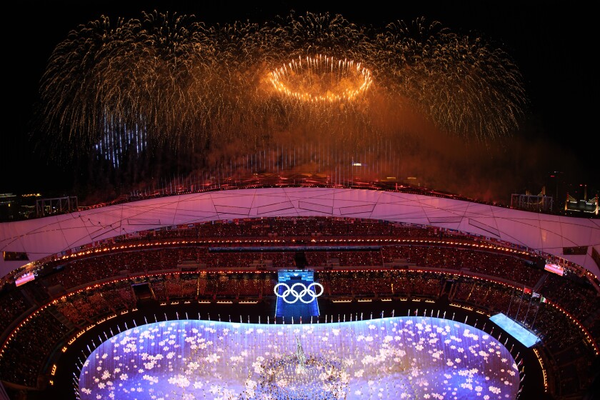 Una pioggia di fuochi d'artificio, con un anello d'oro al centro, è visibile su uno stadio con il logo a cinque anelli delle Olimpiadi 