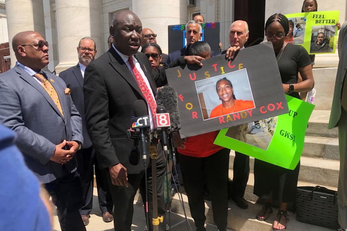 Attorney Benjamin Crump, foreground left, and Doreen Coleman, mother of Randy Cox, hold a poster of Cox, outside a courthouse in New Haven, Conn., Friday, July 8, 2022. Cox, who was being transported in a police van without seatbelts, was paralyzed when the van braked suddenly. His family asked federal authorities Friday to file civil rights charges against the officers involved. (Ben Lambert/New Haven Register via AP)