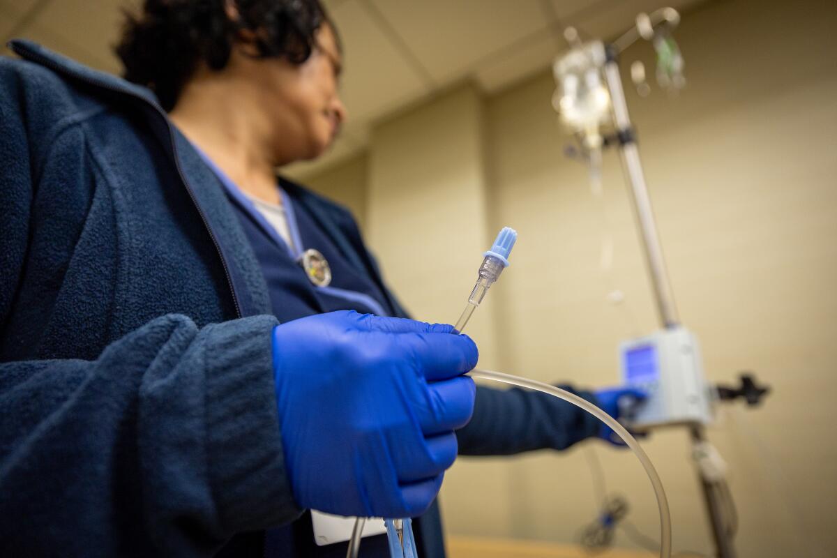 A nurse wearing latex gloves prepares an IV.