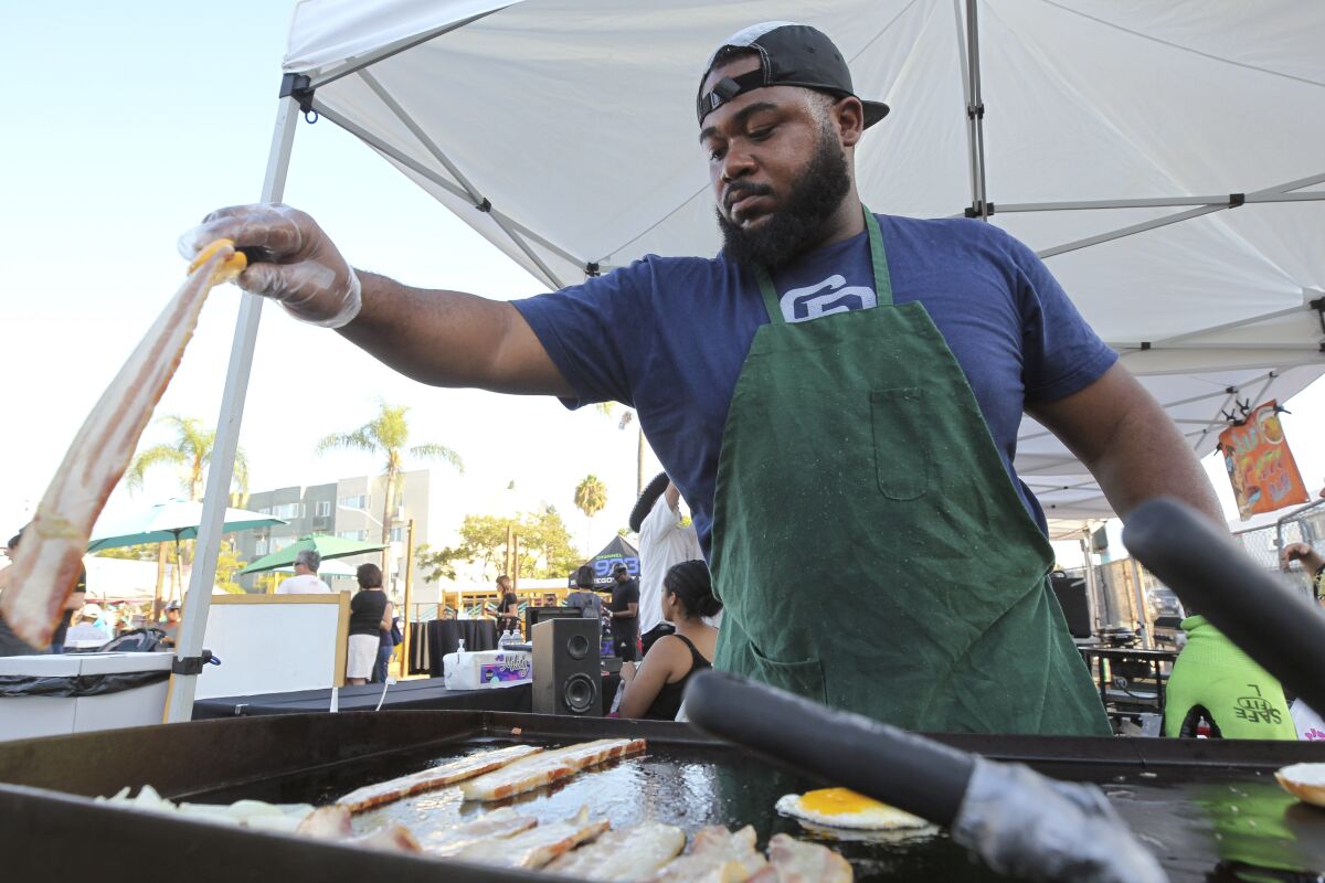 Denezel Bynum cooks bacon as he makes Bully Bagels at his food booth during the City Heights Street Food Festival