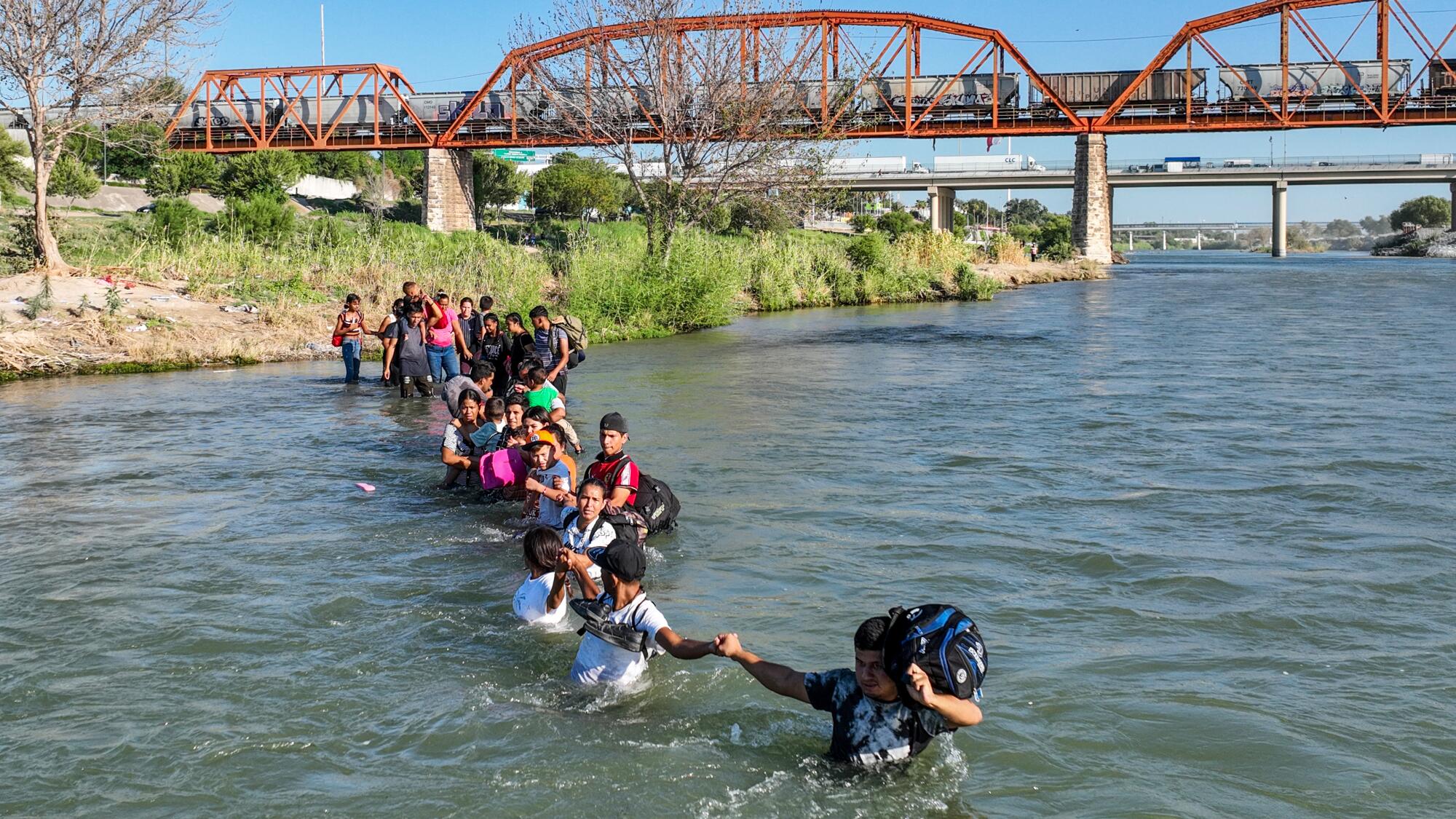 A group of people struggle against the tide as they cross the Rio Grande. 