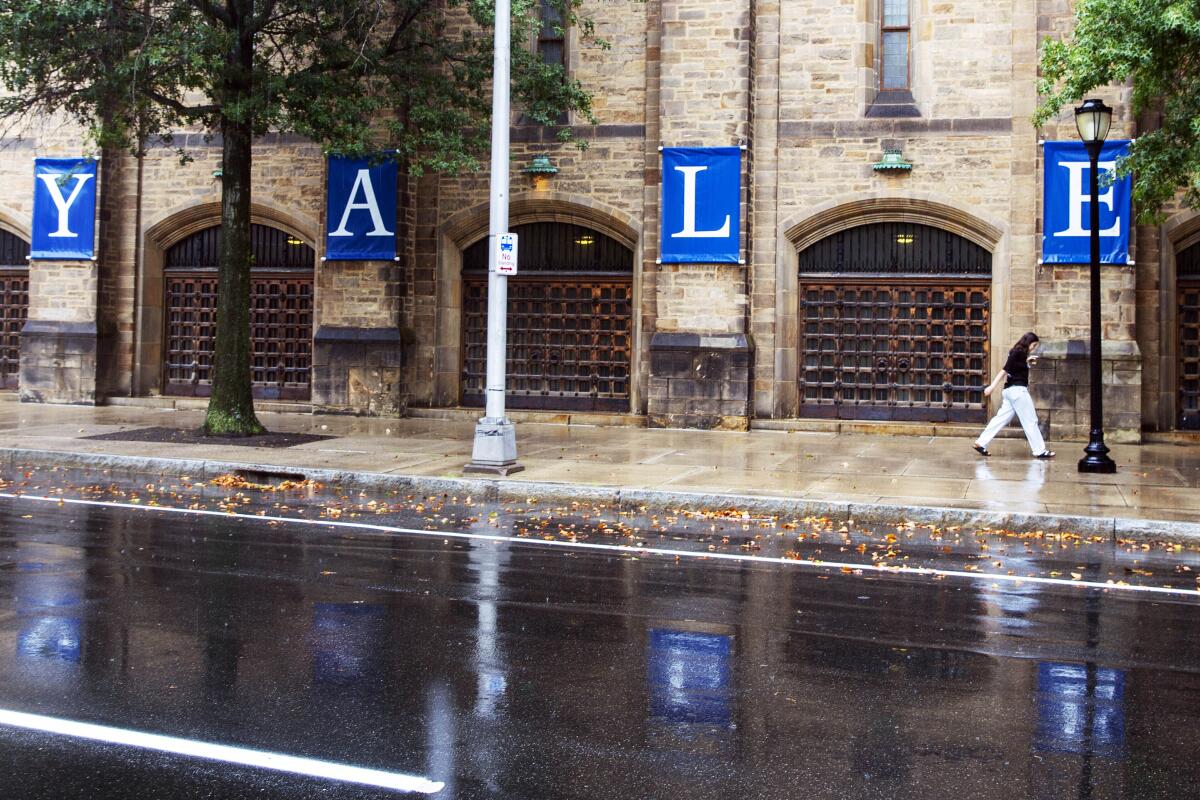 A woman walks by a Yale sign reflected in the rainwater on the Yale University campus.