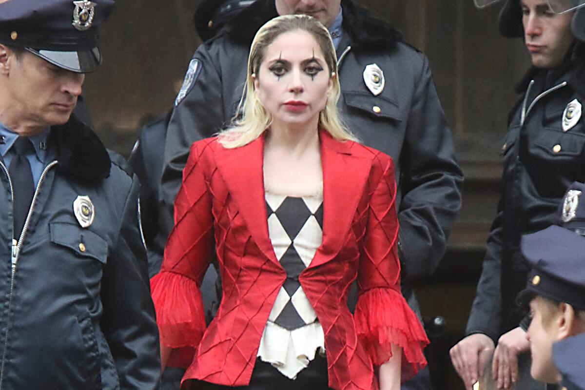 Lady Gaga wears a red blazer, black-and-white blouse and clown makeup while surrounded by men in police uniforms