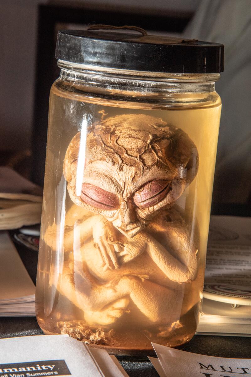 A small alien figure in a glass jar filled with liquid.