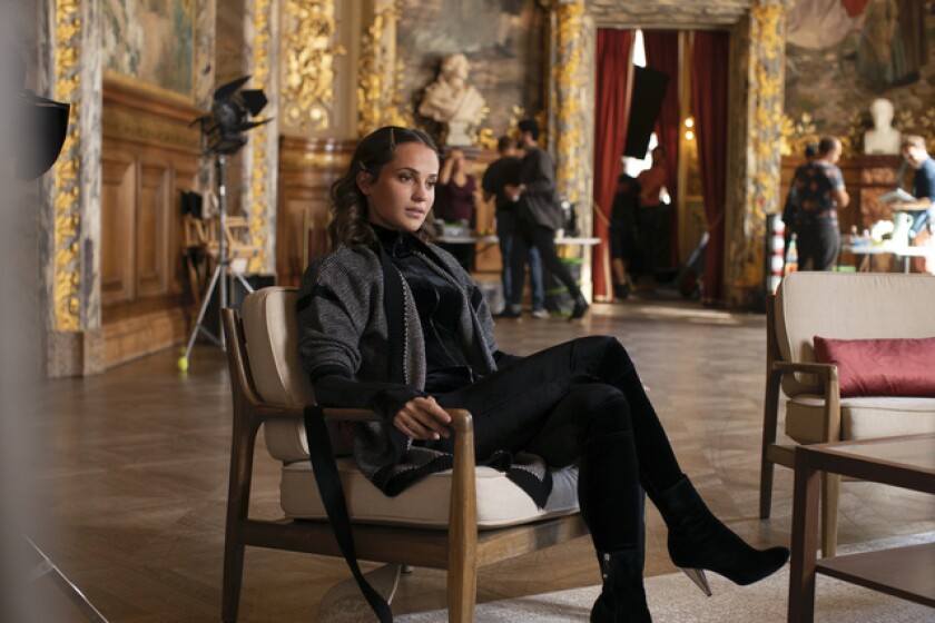A movie star in a black jacket sits crossed-legged in a chair
