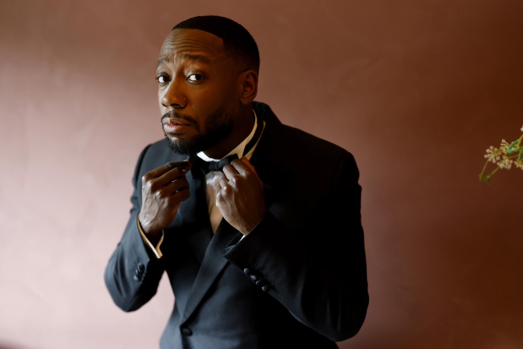 A man in a tuxedo adjusts a black bowtie.