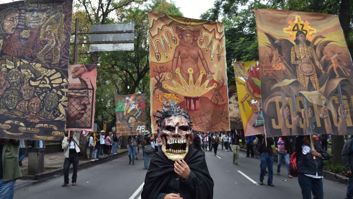 A view of the elaborate Ayotzinapa mask framed by colorful banners that employ indigenous iconography and protest symbols. This image was taken in late September at an anniversary protest in honor of the missing 43.