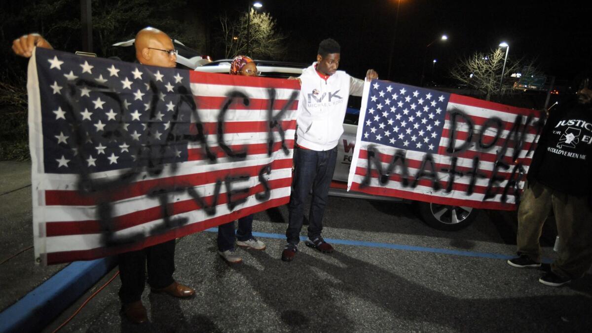 Activists protesting the police shooting of a black man in an Alabama shopping mall hold U.S. flags painted with the words "Black lives don't matter" in Hoover, Ala., on Tuesday.