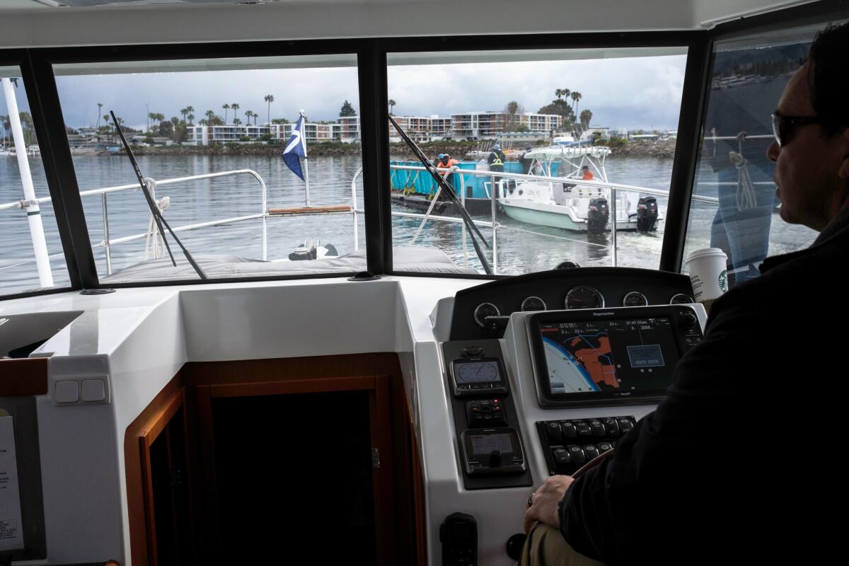 The view of a trash interceptor vessel is framed through the window of a boat, where a pilot stands.