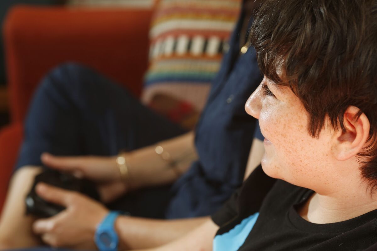 A tween boy smiles while playing video games with his mom.