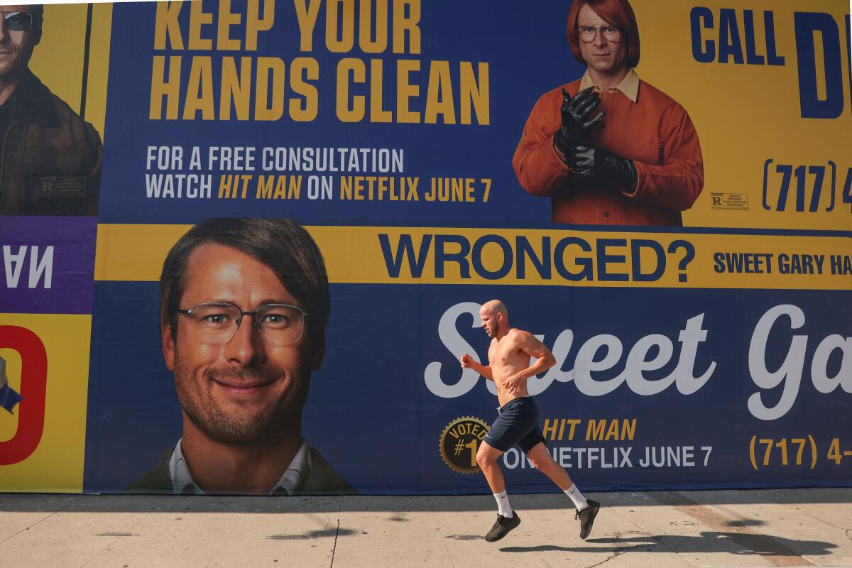 A man jogs by advertisements for Netflix's new film "Hit Man" inspired by L.A.'s famous lawyer billboards.