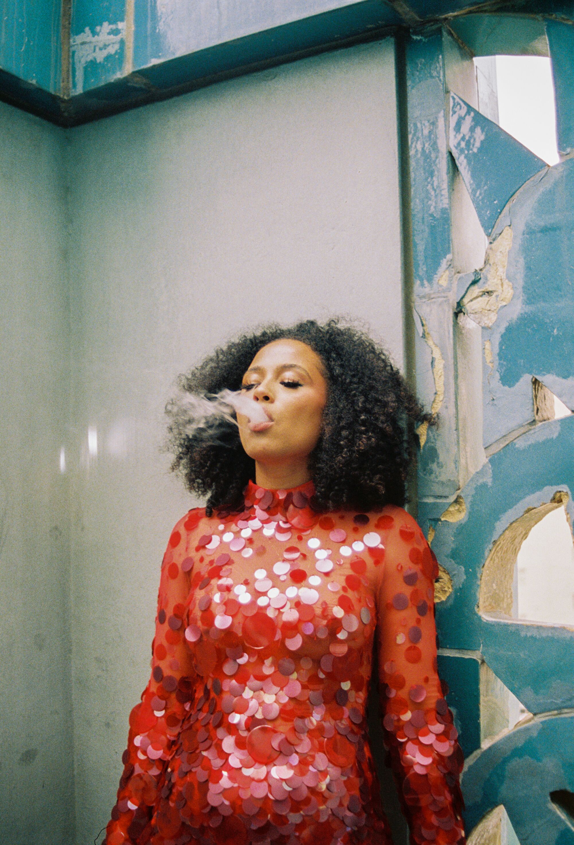 A person wearing a red sequined dress blows out smoke.