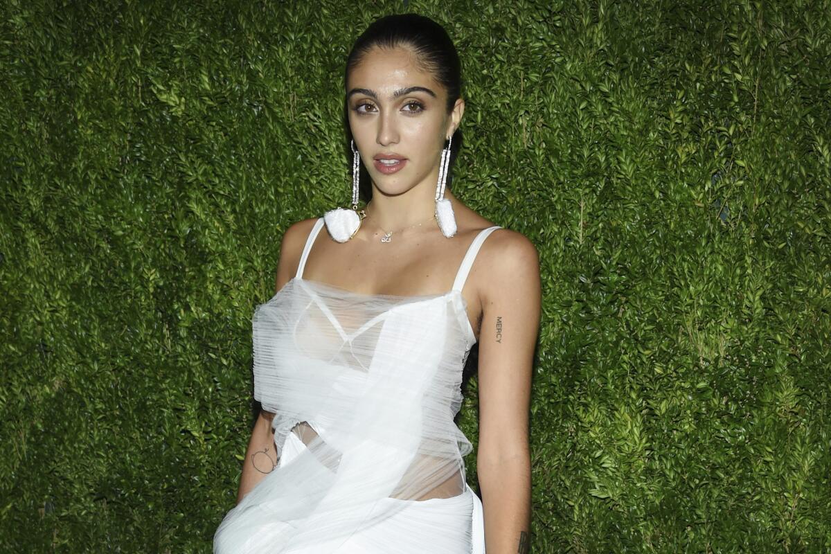 Lourdes Leon in a white dress in front of a grass wall