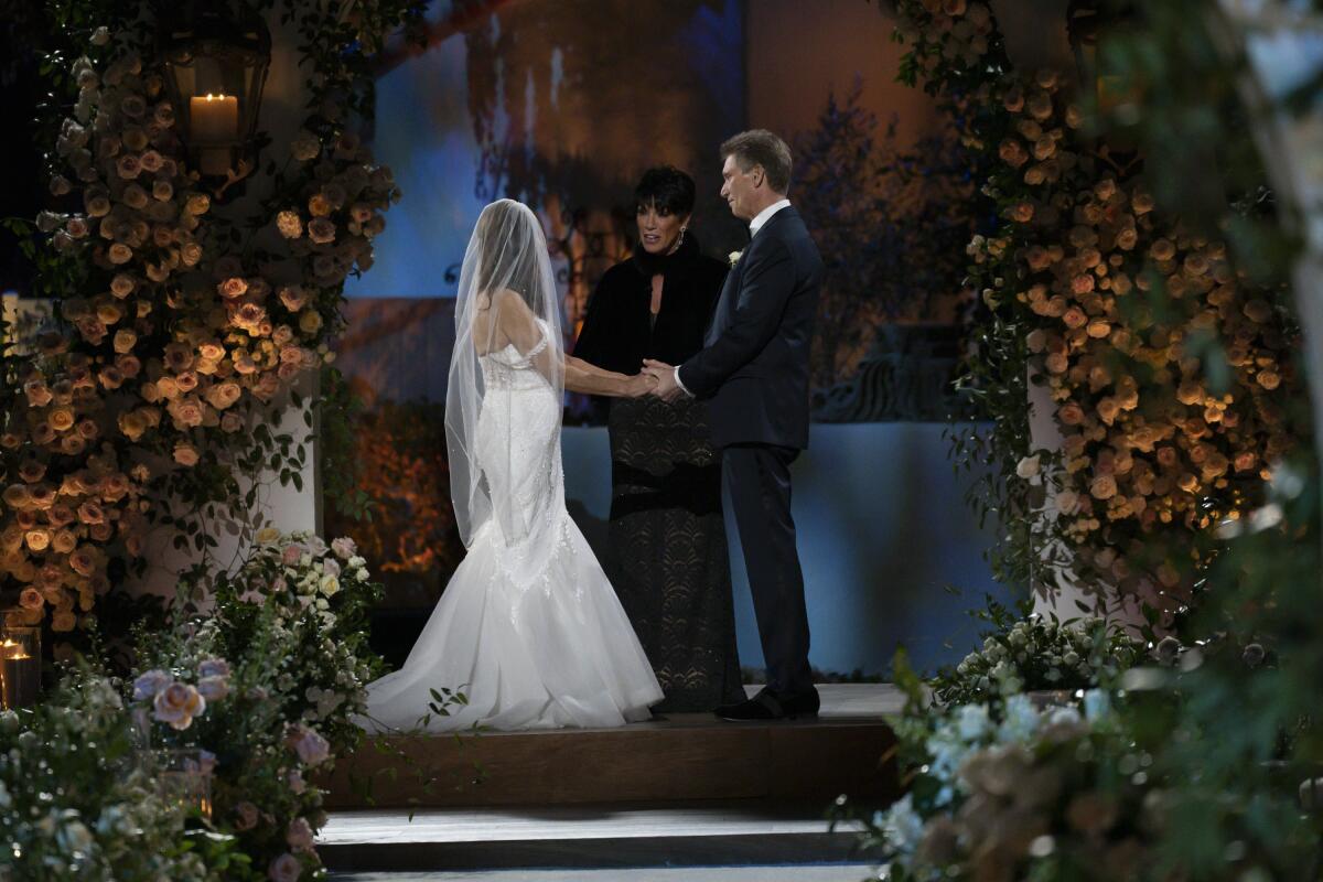 A bride and a groom holding hands at the altar with an officiant dressed in black between them.