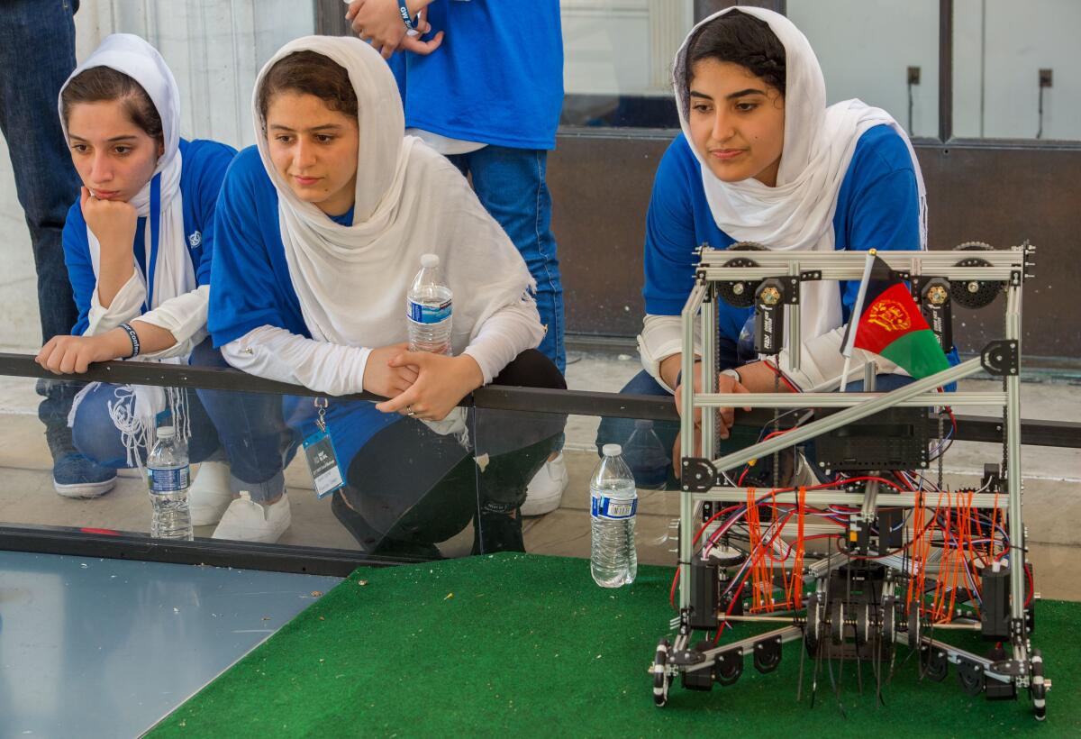 Members of Afghan all-female robotics team kneel on the floor next to their robot