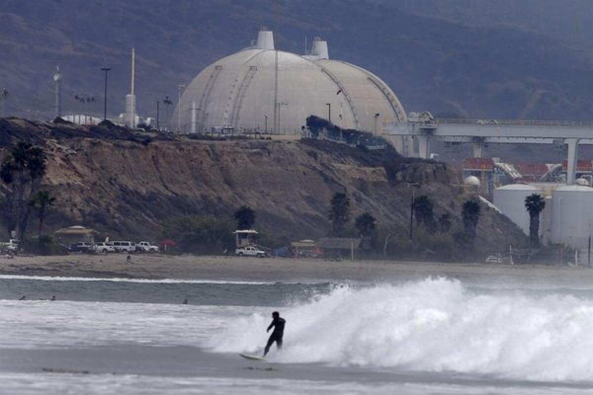 A surfer can be seen near the San Onofre Nuclear Generating Station. Southern California Edison is telling ratepayers that they must pay a portion of the costs to shut down the nuclear plant.