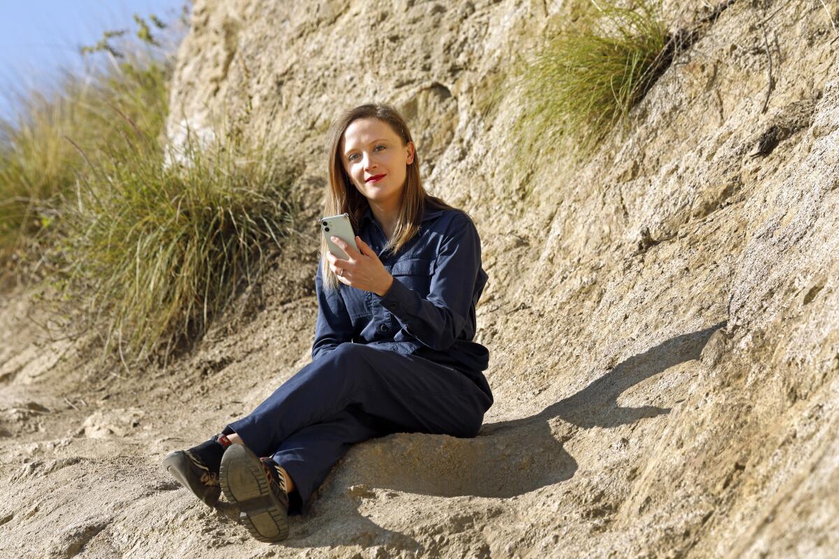 Ellen Reid sits on a rock outcropping, holding her phone.