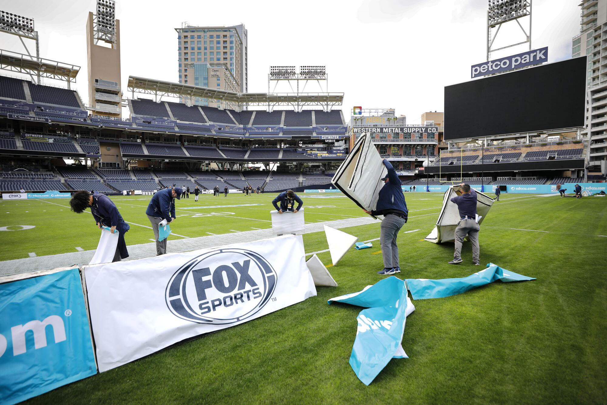Workers take down sideline signage at Petco Park after the Holiday Bowl was canceled.
