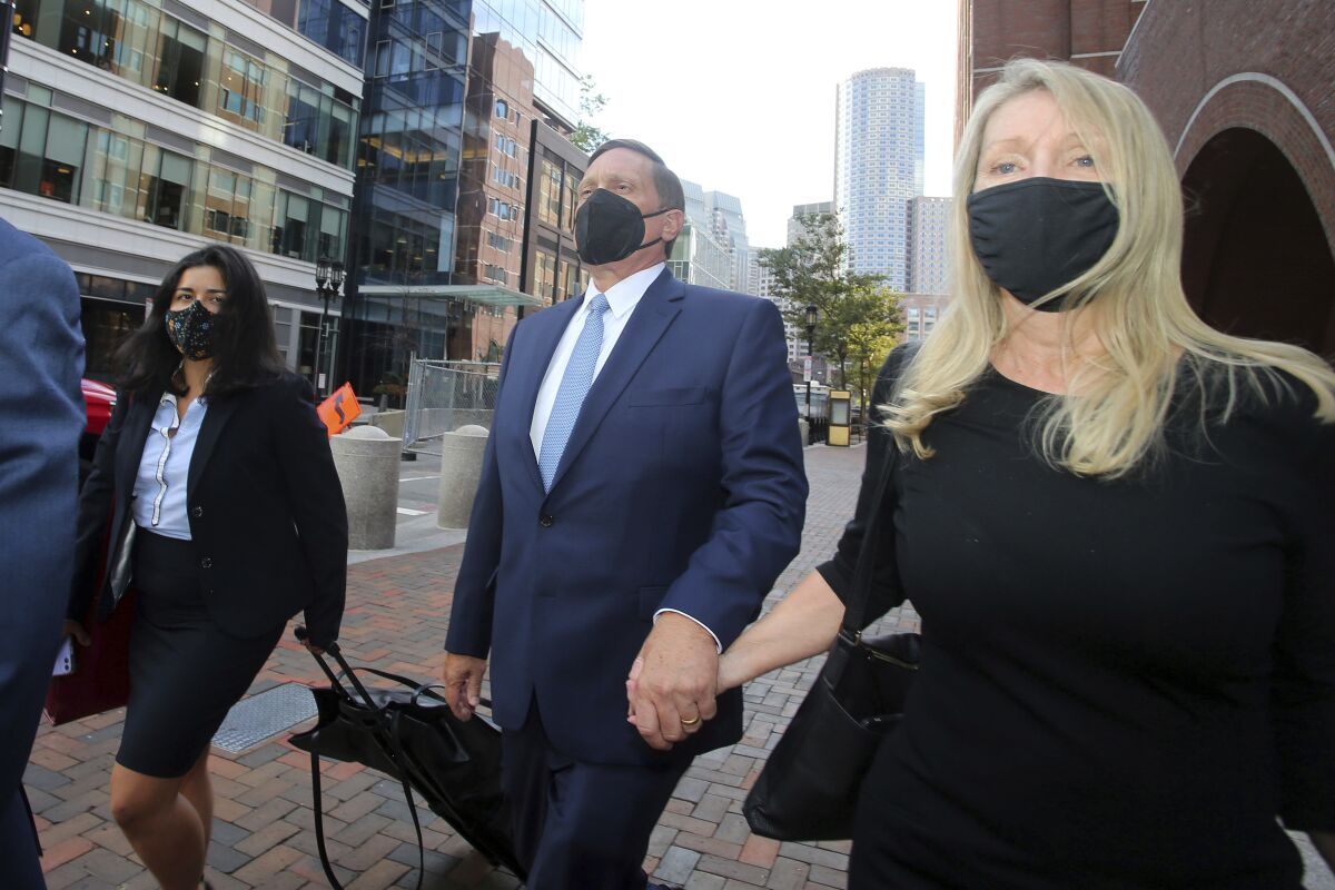 FILE — In this Monday, Sept. 13, 2021 file photo, John Wilson, center, holds his wife's hand, right, as he departs federal court, in Boston. Wilson and another parent, Gamal Abdelaziz, who are the first to stand trial in the college admissions bribery scandal, used lies and money to steal coveted spots at prestigious schools their kids couldn't secure on their own, a prosecutor said Wednesday, Oct. 6, 2021, before jurors decide if the men are guilty. (AP Photo/Stew Milne, File)