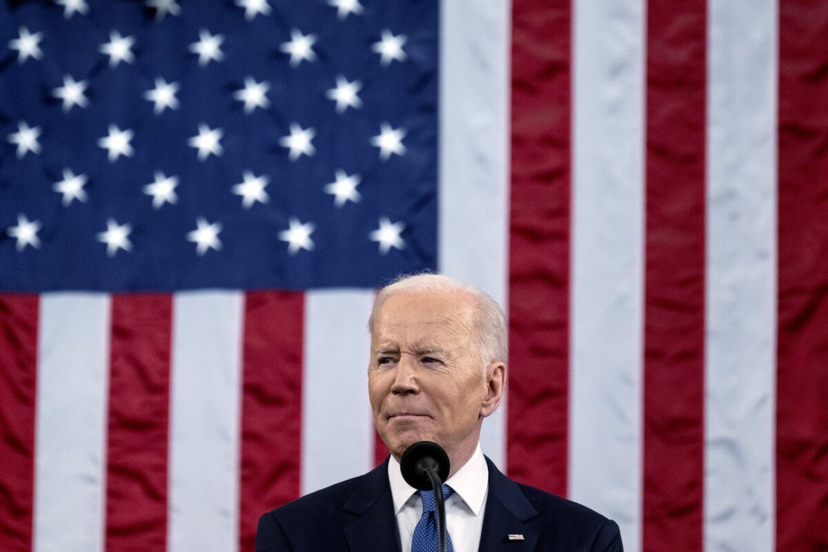 President Biden is seen at a microphone in front of a large American flag