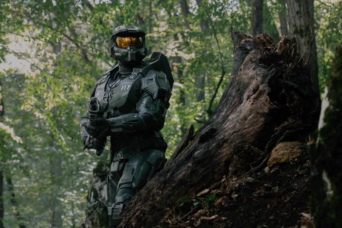 A man in a futuristic body suit holds a gun in a forest.