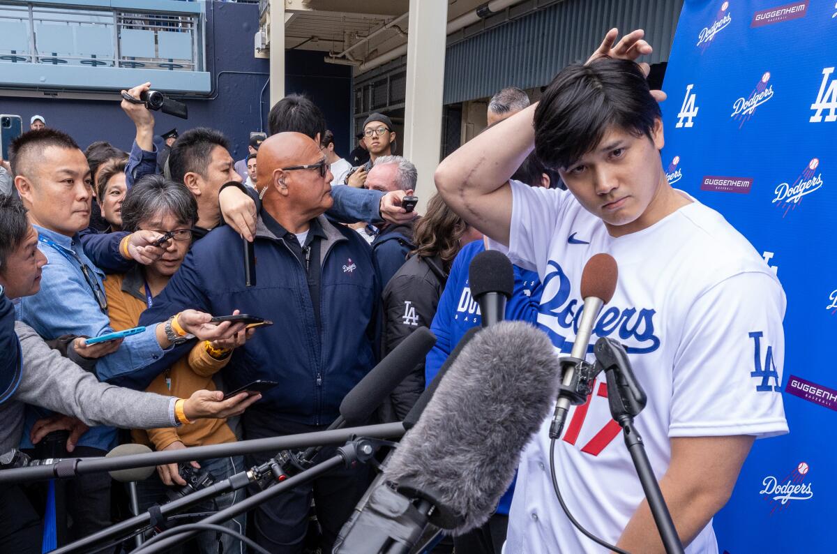 Shohei Ohtani scratches his head while talking with media at DodgerFest 2024.