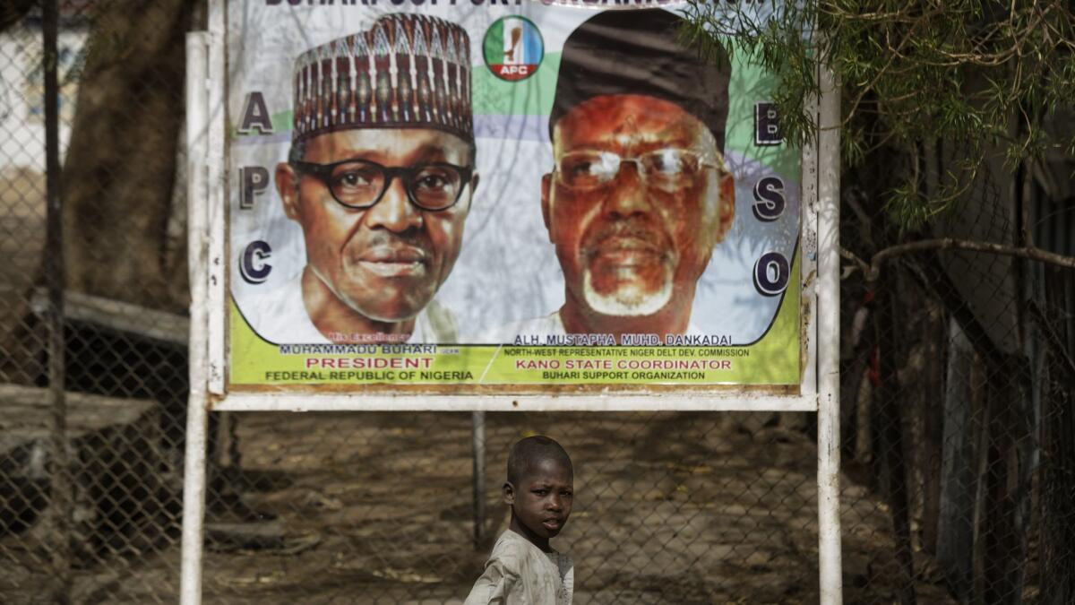 A boy scavenges for items to sell as he walks past a campaign sign for incumbent President Muhammadu Buhari, left, and local party official Mustapha Dankadai in Kano, northern Nigeria.