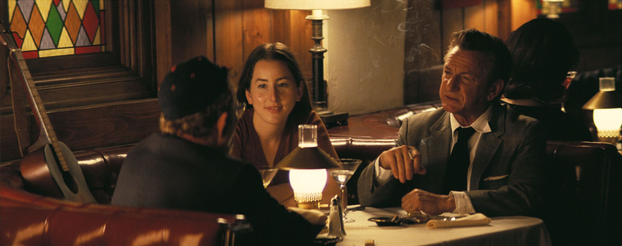  A young woman and two older men chat at a restaurant table in "Licorice Pizza."