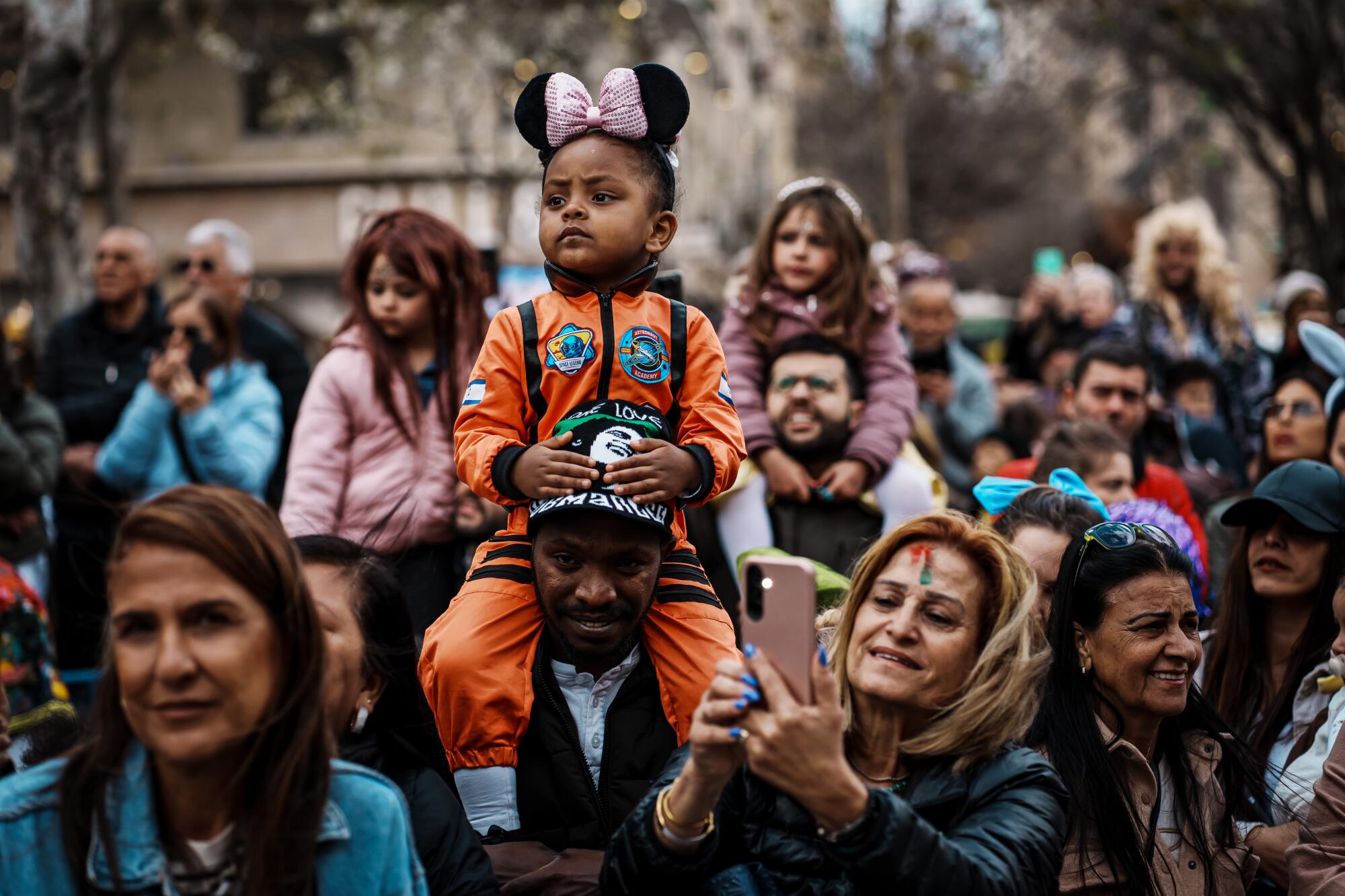 当他们参加耶路撒冷的游行时，3 岁的加布里埃拉·詹伯 (Gabriella Jember) 打扮成宇航员，坐在她父亲的肩膀上。